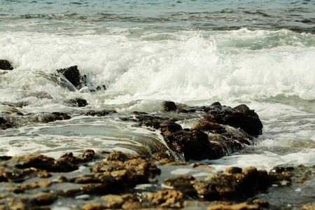 Beautiful grey sea or ocean stormy waves with white foam and ripples splash against black stony, rocky, shore on sunny day on natural backgroundの写真素材