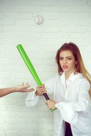young pretty woman or cute sexy girl with beautiful long hair and red lips on adorable serious face in fashionable white shirt holds green baseball bat or racket and ball on brick wall backgroundの写真素材