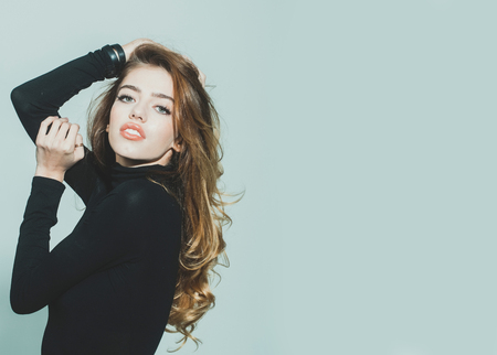 young pretty woman or cute sexy girl with long beautiful curly blonde hair and red lips on adorable face in black jumper on grey background, copy spaceの写真素材