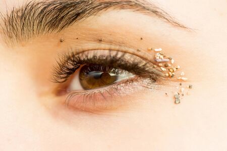 Pretty female eye, brown color look, with eyelashes and eyebrow, natural granular sand on eyelids on young skin backgroundの写真素材