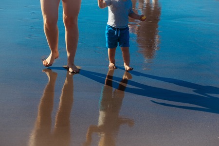 Female and child barefoot legs and footprints reflected in wet sand surface on sunny summer day on...