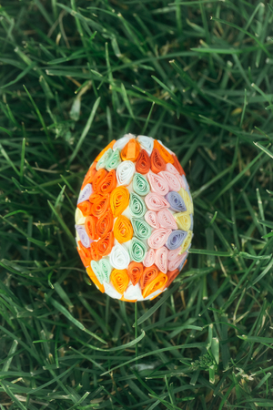 Easter egg decorated with colorful paper in quilling technique on green grass green background