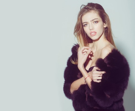 young pretty woman or cute sexy girl with long beautiful curly blonde hair and adorable face in black fur vest or waistcoat on grey background, copy spaceの写真素材