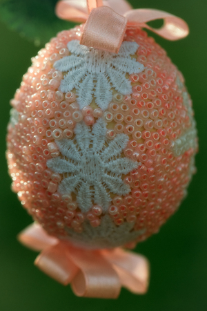 Easter egg decorated with white flowers pink seed beads and ribbons on blurred green backgroundの写真素材