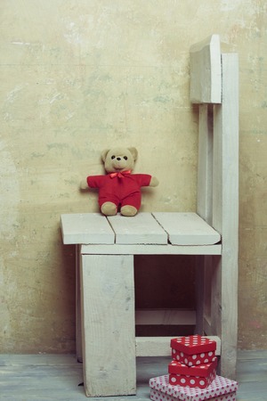 colorful valentines day teddy bear toy, present or gift boxes on white vintage wooden chair on textured wall backgroundの写真素材