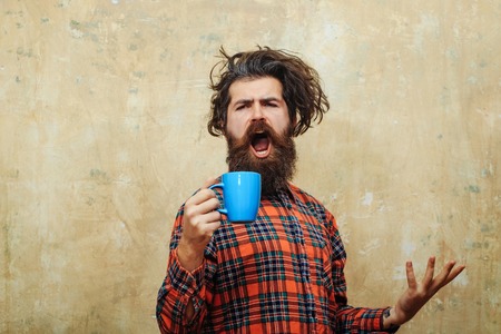 singing bearded man, caucasian hipster, with long beard and moustache pulling stylish fringe hair, haircut, in red plaid shirt with blue cup on abstract pink wall backgroundの写真素材