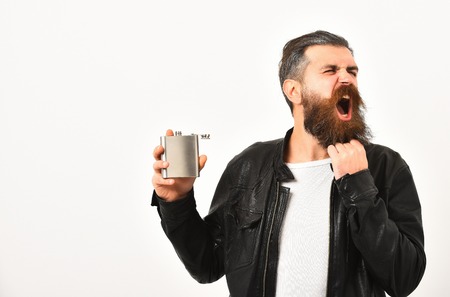 bearded man, long beard, brutal caucasian hipster with moustache holding metallic flask, jar for alcoholic drink, has shouting face, in black leather jacket isolated on white background, copy spaceの写真素材