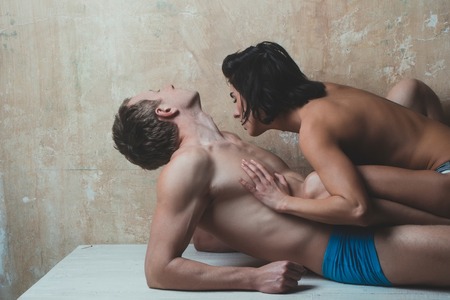 young couple of handsome macho man in blue pants with muscular body and pretty woman or sexy girl with naked chest on textured wall background laying on tableの写真素材