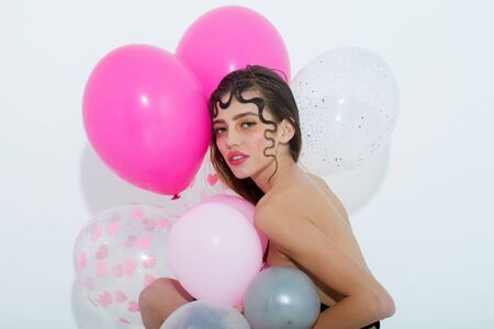 Pretty girl or cute woman with curly lock of hair, hairstyle, sexy rosy lips, stylish makeup, on young face with party balloons, colorful, pink, hearts has bare shoulder isolated on white backgroundの写真素材