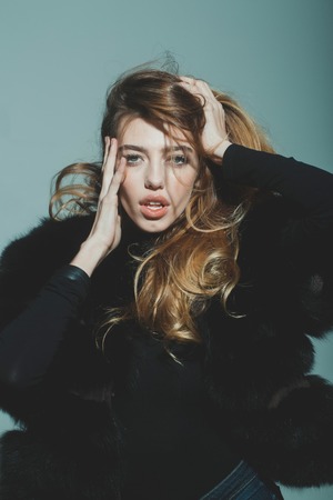 young pretty woman or cute sexy girl with long beautiful curly blonde hair and adorable face in black fur vest or waistcoat on grey backgroundの写真素材