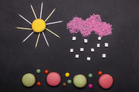 colorful macaron, tasty cookies, biscuits or meringue pastry with marshmallow, zephyr and dragee, rainy cloud sprinkles sweets with birthday cake candles in shape of sun on grey backgroundの写真素材