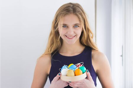 colorful painted easter eggs in box, traditional spring holiday food. celebration and decoration. happy girl with long blonde hair and smiling cute face on white background.の写真素材