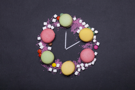 colorful macaron, tasty cookies, biscuits or meringue pastry with marshmallow, zephyr and dragee, sprinkles sweets with birthday cake candles in shape of clock on grey background, copy spaceの写真素材