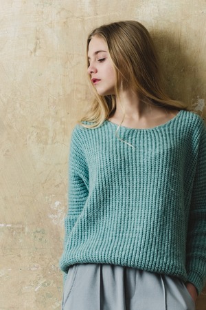 Pretty girl or cute young woman with blond hair and adorable face in blue sweater and fashionable grey culottes pants on textured wall backgroundの写真素材
