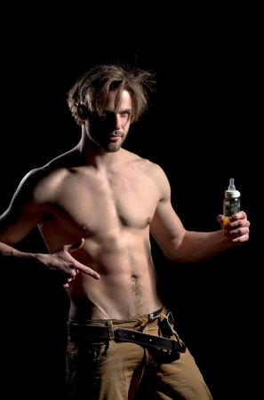 Handsome man, unshaven macho or bodybuilder, pointing finger at feeding baby bottle with teat, guy with stylish hair, sexy naked muscular torso with six packs, abs, biceps, triceps on black backgroundの写真素材