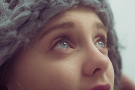 Pretty girl or cute young woman with blond hair and adorable face looking up in fashionable grey hat has big blue eyes on white backgroundの写真素材