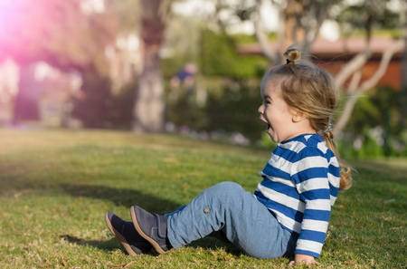 Excited cute baby boy, small child with long blond hair in blue striped clothes shouting and playing on green grass on sunny summer day outdoors on natural background. childhood and vacation conceptの写真素材