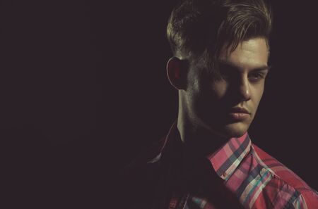 Handsome man or young caucasian macho with stylish haircut, hair, posing with serious face in red plaid tshirt, casual wear on black background, copy spaceの写真素材