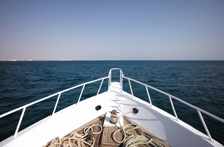 White boat or ship, vessel heading to horizon in sea or ocean water on sunny day on blue sky background. Idyllic summer vacation, traveling and transport, sport, hobby, fishing and yachtingの写真素材