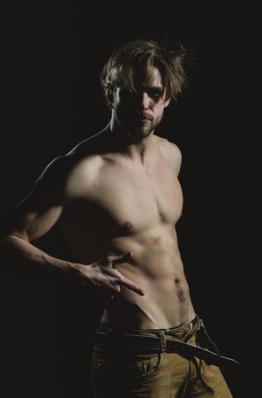 Handsome man or unshaven macho, bodybuilder, with stylish blond hair, haircut, sexy, naked, muscular torso with six packs and abs, biceps, triceps unfastening belt on black backgroundの写真素材