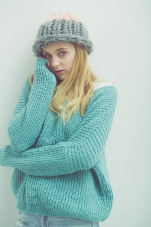Pretty girl or cute young woman with blond hair and adorable face in fashionable blue sweater and hat on white backgroundの写真素材