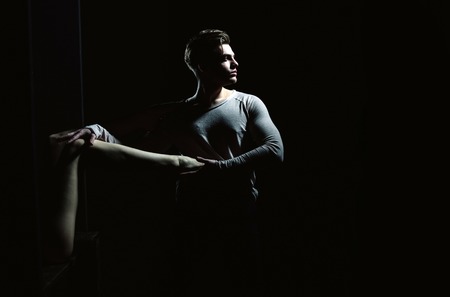 Handsome man or young caucasian macho with stylish haircut, hair, posing with sexy, naked, female leg in hands on black background, copy spaceの写真素材