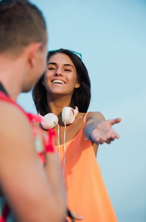Happy girl or beautiful woman with cute smile and brunette hair in sexy orange shirt smiling and reaching for handsome man on sunny, summer day on blue sky. Helping hand and relationshipの写真素材