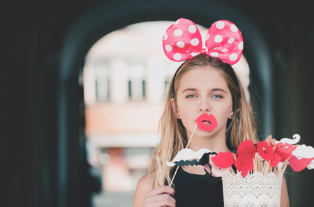 Funny pretty girl or young woman, teenager, with long, blond hair posing with cute mouse ears and paper red lips. Decorative props on sticks. Holiday, birthday, anniversary celebration. Fun partyの写真素材
