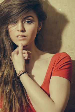 Pretty girl or cute, sexy woman with beautiful, long, blond hair, hairstyle, in red tshirt on beige wallの写真素材