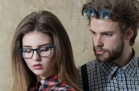 Young nerd couple of students in geek glasses. Pretty girl or beautiful woman with long hair and handsome man with beard in checkered shirts on beige background. Education and knowledgeの写真素材