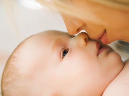 Young mom woman kissing face of her little son newborn baby laying on light coverの写真素材