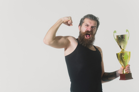 bearded man, long beard, brutal caucasian hipster with moustache in black vest holds gold champion cup with happy face on grey background, unshaven guy, copy spaceの写真素材