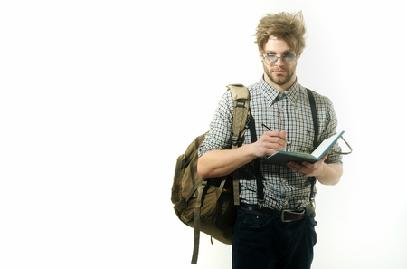 traveler notes in paper notebook, handsome man with beard and stylish hair, haircut, with backpack in checkered shirt, jeans with suspenders, glasses writing with pen isolated on white backgroundの写真素材