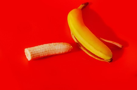 Vitamin banana, ripe peeled fruit, and yellow skin on red background. Healthy eating and dietingの写真素材