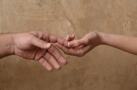 Love and care. Male and female hands touching each other on abstract cement wall on beige backgroundの写真素材