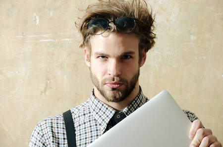 Education and technology. Handsome man or smart, male student, businessman, with beard in nerd glasses on head with stylish, blond hair, and checkered shirt with suspenders holding laptop, computerの写真素材