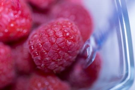 Red raspberries, ripe, fresh and delicious berries or fruit in plastic bowl on blurred background. Healthy food and dietingの写真素材