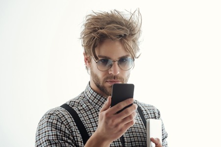 Handsome man or male student, businessman, with beard and stylish, blond hair, in nerd glasses with smartphone and laptop computer. Using technology, internet surfing and video conferencingの写真素材