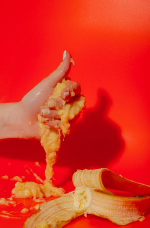 banana, ripe mellow fruit and peeled yellow skin in female hand squeezing juice or squash on bright orange background. Vitamin and healthy eatingの写真素材