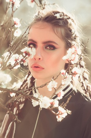 woman in beautiful spring flower blossom in garden with fashion makeup on summer natural background,...