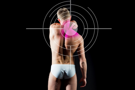 target on man suffers from backache standing over black background, A guy with bare body and muscular torso in white pants. Concept with Healthcare And Medicine.の写真素材