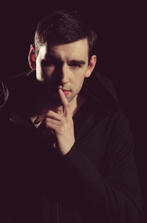 man or elegant handsome guy in stylish coat on black background, holding finger near mouth has...
