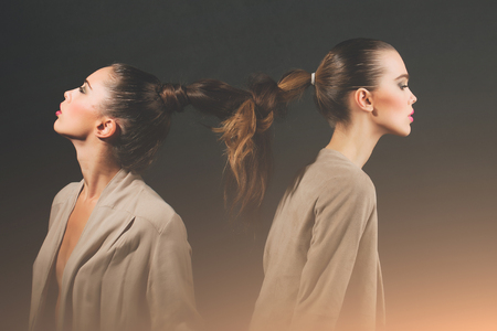 Two cute girls or adorable women, stylish models, with braided or tied, beautiful, brunette, healthy, long hair into braid or plait on grey background. Friendship and friendsの写真素材