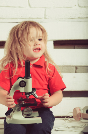 happy blonde child or small baby boy with microscope and headset on white wooden backgroundの写真素材