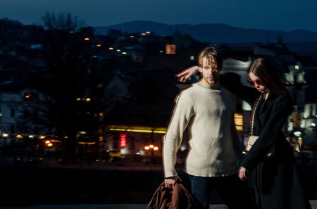fashion couple of young man and girl in coat and sunglasses in evening outdoor on blurred night city illuminated background, motion effect, copy spaceの写真素材