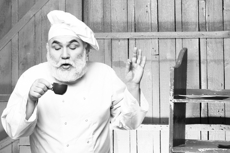 Bearded man cook in chef hat drinking coffee on wooden background, black and whiteの写真素材