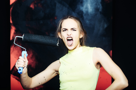 pretty shouting woman painter or dirty cute sexy girl builder with roller, building tool painting pink wall with black color, in yellow vest. repair and construction conceptの写真素材