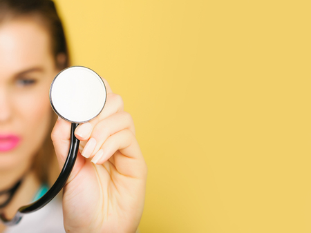 Modern stethoscope, medical acoustic device, with small disc resonator in female hand of blurred, pretty doctor or nurse, cute woman, girl on orange background. Healthcare and examination, copy spaceの写真素材