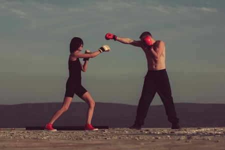 Romantic couple of boxers fighting for love on blue sky. Happy pretty girl or cute woman boxing with handsome man in gloves on sunny, summer day on nature. Sport, energy and competitionの写真素材