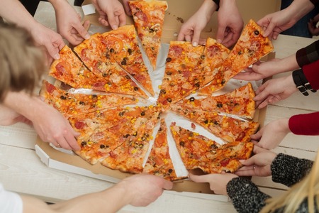 pizza and human hands taking delicious, cooked, big, fat dish, fast food, slices from delivery box package. Italian cuisine. Obesity and dietary problemsの写真素材